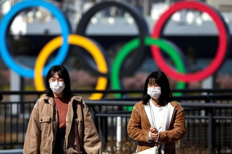 Dua warga berjalan di depan logo olimpiade di Tokyo, Jepang. (REUTERS via ABC INDONESIA)