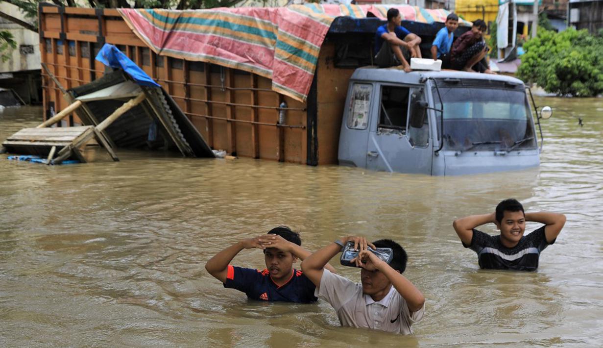 Warga menyebrangi truk yang terendam banjir saat banjir di Lhoksukon, Aceh Utara, 3 Januari 2022. Badan Penanggulangan Bencana Daerah (BPBD) Aceh Utara mancatat banjir telah merendam 14 Kecamatan di daerah tersebut. (Foto: Azwar Ipank/AFP)