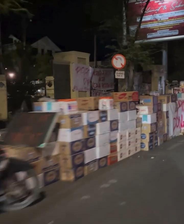 Pantauan Nukilan.id pada Minggu (31/8/2025) memperlihatkan ratusan kotak air mineral sudah berjejer di depan DPRA sebagai hasil sumbangan masyarakat. (Foto: Nukilan)