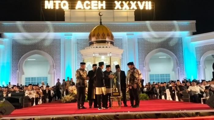 Wakil Gubernur Aceh, Fadhlullah, menyerahkan piala bergilir yang diterima Bupati Aceh Besar yang tampil juara umum pada MTQ Aceh XXXVII di mimbar utama komplek Bupati Pidie Jaya, Jumat (7/11/2025) malam. (Foto: SerambiNews)